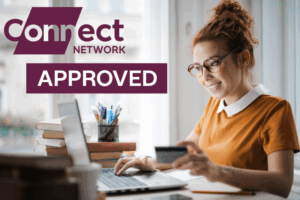 A woman with red hair tied in a bun is smiling while sitting at a desk, using a laptop and holding a credit card. She is wearing glasses and an orange top. On the desk are books and a pen holder with stationery. In the top left corner, there is branding that reads “Connect Network” and a banner that says “APPROVED.” This represents FCA-Regulated Mortgage Brokers