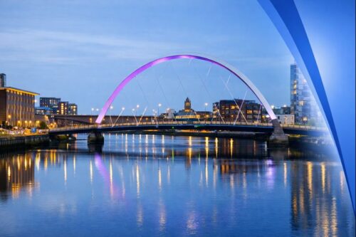 Aerial evening view of Glasgow featuring the Clyde Arc bridge over the River Clyde, with city lights reflecting on the water and a subtle Connect Mortgages blue gradient fading in from the right side. This is to represent Mortgage Advisers in Glasgow