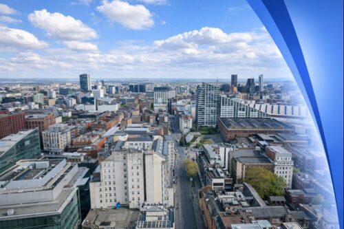 Aerial view of Manchester city centre showing modern and historic buildings under a partly cloudy sky, with a subtle Connect Mortgages blue gradient fading in from the right side. Mortgage Advisers in Manchester