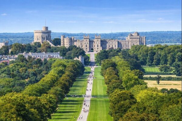 Historic castle in the distance with a long straight path lined by trees and people walking through a large green park.
