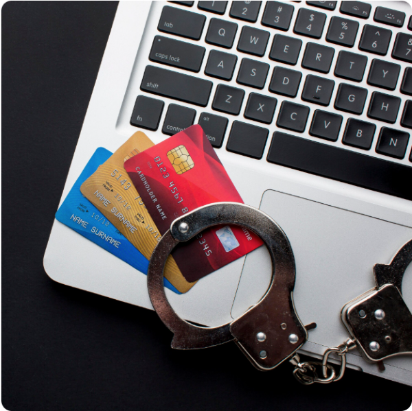 Close-up of a laptop keyboard with two bank cards partially tucked underneath a pair of metal handcuffs, symbolising credit card fraud or financial crime.