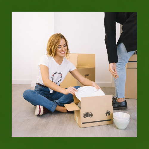 A smiling woman sits cross legged on a wooden floor unpacking white plates from a cardboard moving box, while another person stands nearby, with a green branded border surrounding the image. Gary Poyntz Mortgages and Protection Limited