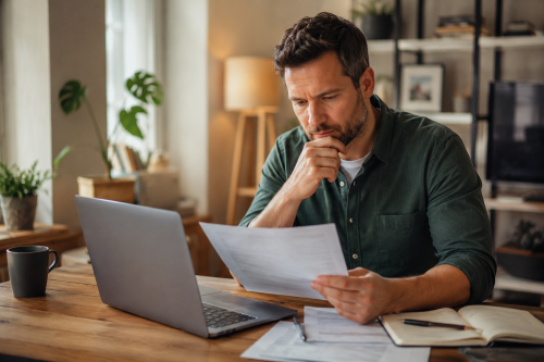 A man reviewing financial paperwork at home beside a laptop, representing mortgage protection planning, income protection advice and the importance of safeguarding household finances. Protection Mortgage Brokers