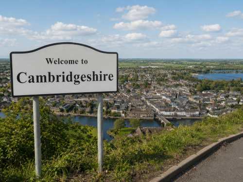 White “Welcome to Cambridgeshire” road sign overlooking a riverside town, bridge, green fields, lakes and open countryside under a bright blue sky. Why Move to Cambridgeshire