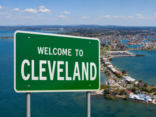 Welcome to Cleveland road sign overlooking a coastal town, marina, blue water, shoreline homes, and distant hills. Why Move to Cleveland