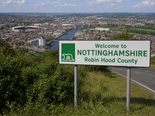 Welcome to Nottinghamshire road sign overlooking a cityscape, river, stadiums, roads, green fields, and countryside, with no cars visible. Why Move to Nottinghamshire
