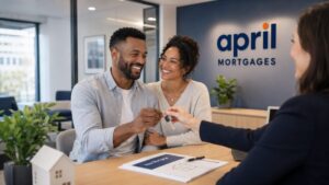 April No Deposit Mortgage hero image showing a diverse couple in an office meeting, smiling as they receive keys from an adviser, with the April Mortgages logo displayed on the back wall.